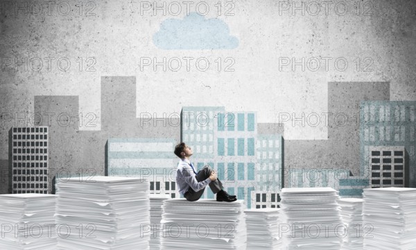 Thoughtful businessman looking away while sitting on pile of documents with drawn cityscape on