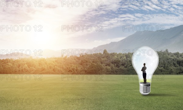 Young businesswoman trapped inside of light bulb on green field