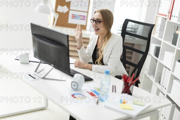 A beautiful young blonde girl in a white jacket and black blouse is working in the office. photo
