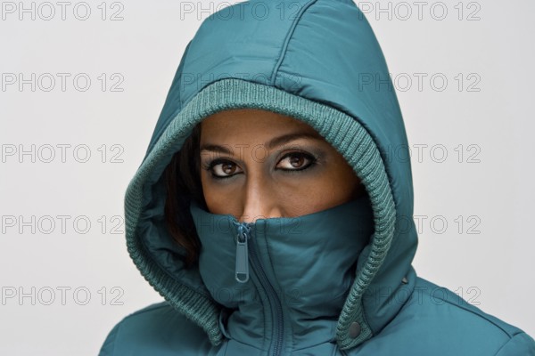 A young woman wearing a green winter coat using the hood to cover her head so that only her eyes