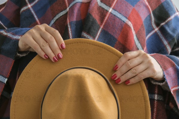 Stylish red female nails. Woman in poncho holding brown trendy hat. Modern Beautiful manicure.