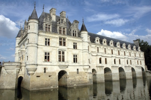 Historic stone castle with turrets and windows, reflected in surrounding water under a blue sky.