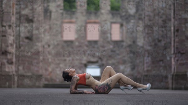 Woman in sporty pose and high heels lying on the ground in front of an old ruin, Staged outdoor