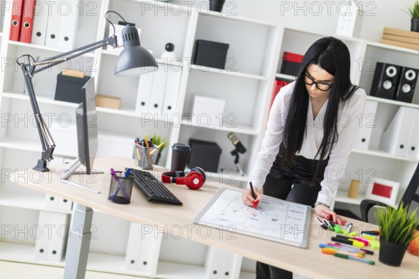A young girl with glasses, wearing a white blouse and black trousers, works in the office. The girl