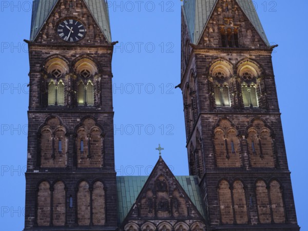 Detailed view of two Gothic church towers with clocks, illuminated in the soft evening mood,
