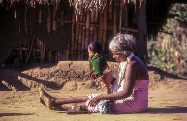 A jenu kurumba tribal old woman with her grandson. Baby urinating in Nagarahole tribal settlement
