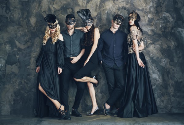 Group of people in masquerade carnival mask posing in studio. Beautiful women and men wearing
