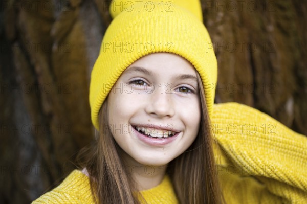 Cute and happy teenage girl with braces smiling at camera in yellow clothes in park. Concept of