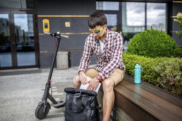 Handsome hipster style bearded man works online freelancer, pulls out laptop with backpack and