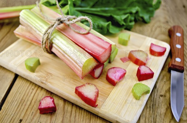 Bundle of stalks rhubarb, cut pieces of rhubarb with a sheet and a knife on a wooden boards