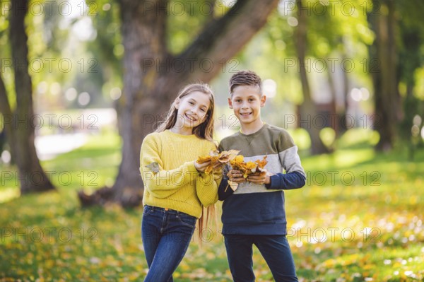 Happy Caucasian siblings enjoying in autumn day in park, sunny weather. Kids having fun holding