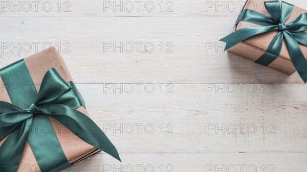 Two gift boxes in craft wrapping paper and green satin ribbon on white wooden table, copy space in