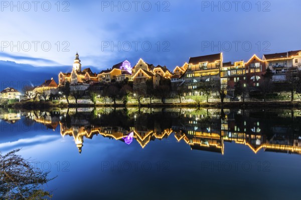 Christmas illuminated house facade of Frohnleiten reflected in the river Mur, blue hour,