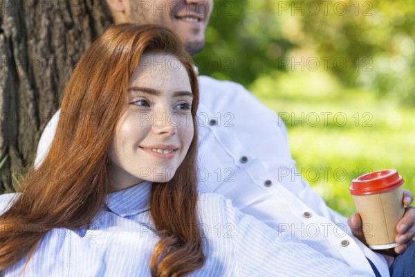 Young couple relaxing under tree in summer park on sunny day. Happy couple in love spend time