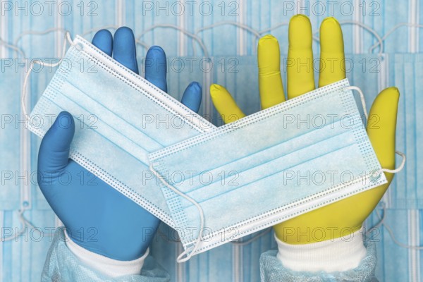 Doctor holds medical face mask in blue glove in one hand and other surgical face mask in yellow