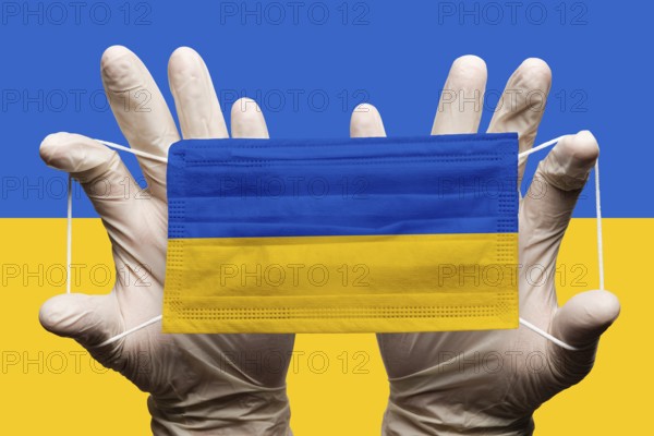 Doctor holding in white gloves protection medical face mask with National flag of Ukraine