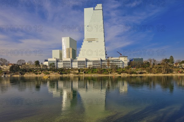 Towering buildings are reflected in the calm water under a blue sky, pharmaceutical company Roche,