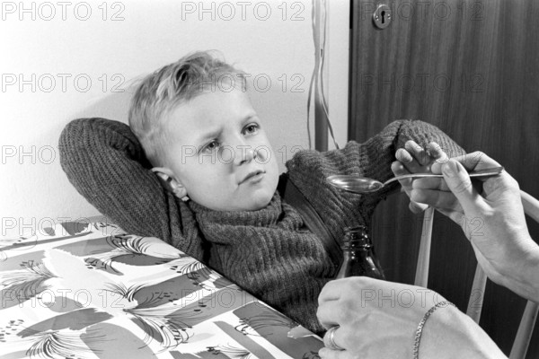 A boy is sick and won't take his medicine. His mother holds out a spoon and waits for him to gape