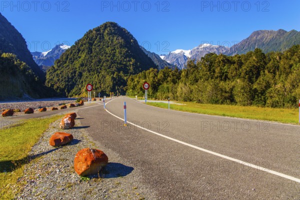 Snowy peaks of rocks are visible in the distance. Wonderful summer day. Great highway among fields,