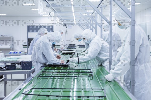 Factory workers in white lab suits and face masks, producing tv sets on a green assembly line with