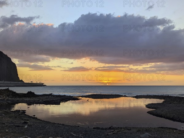 Sunset over the ocean, with striking reflections on wet sand and dramatic clouds in the sky.
