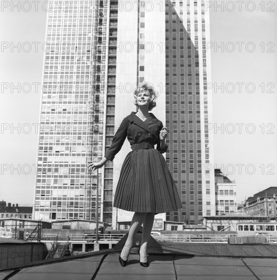 In the 1950s. A woman modelling a 1950s outfit with a jacket and skirt in matching dark. In the