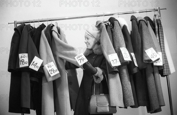 Great discounts of outerwear in the 1960s. A woman stands by a clothes rack, choosing from