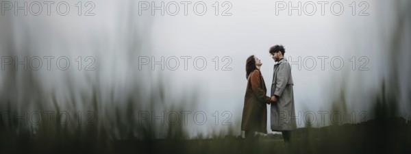 A couple standing apart in a field on an overcast day, holding hands, conveying a sense of