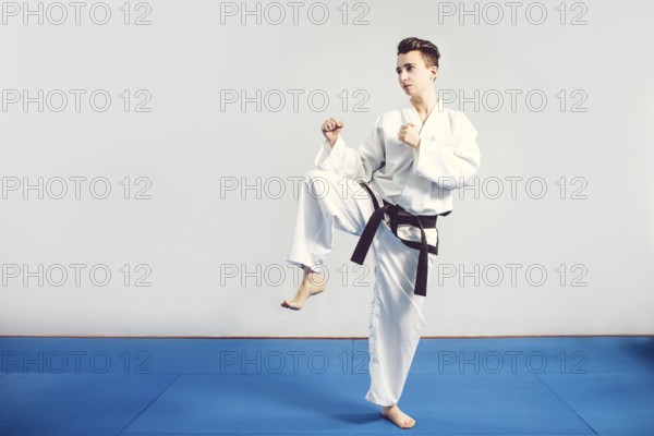 Girl in karate suit kimono in studio at grey background. Female child shows judo or karate stans in