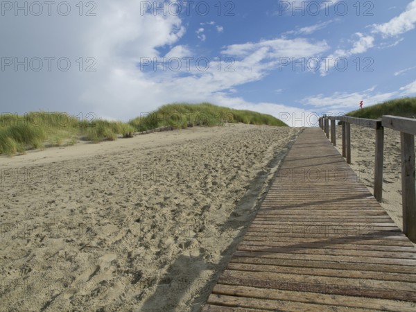 A long wooden walkway leads up sandy dunes, with a sky of clouds and blue, Juist, East Frisia,