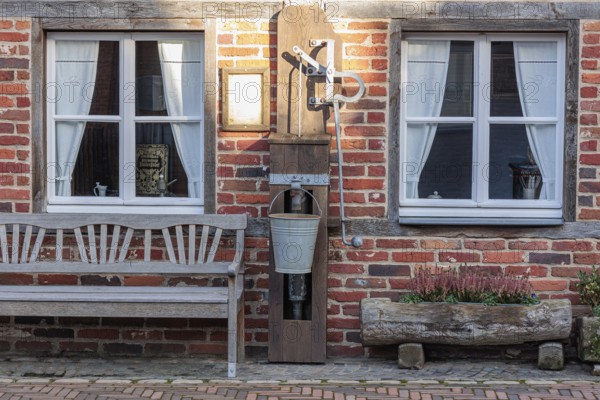 Rustic brick wall with two windows, old water pump and bench against a rural backdrop, gemen,