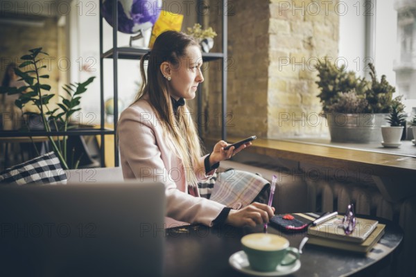 Woman sitting coffee shop wooden table, drinking coffee and using smartphone. Woman Using Phone In