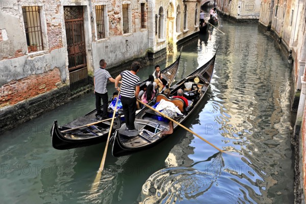 Venice, Veneto, Italy, Europe, Gondolas manoeuvre through a narrow canal, surrounded by old brick
