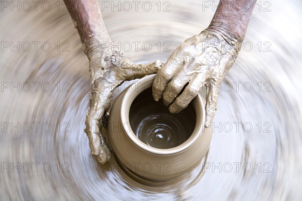 Pottery, artist muddy hands making clay pot giving shape on spinning wheel, semi urban village