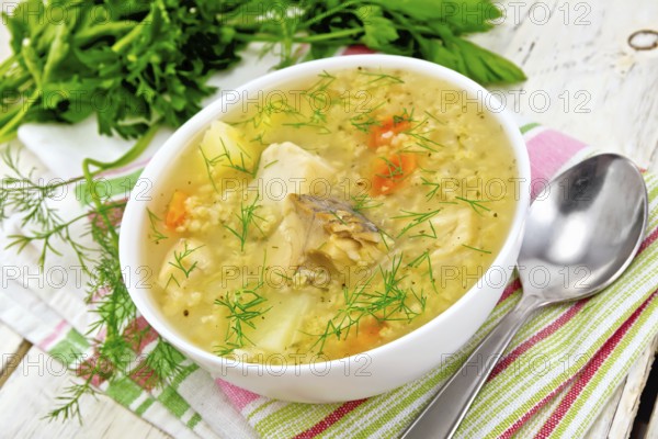 Soup fish kulesh with millet, potatoes and carrots in a white bowl on a napkin, parsley, dill on a