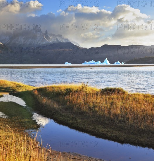 Gray lake and snow-capped mountains. Blue iceberg floating in the distance. Warm summer sunset