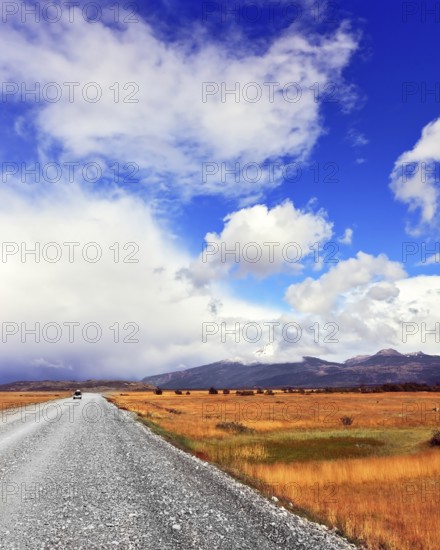 The dirt road in the endless pampas. Strong wind drives the clouds. See the mountains on the