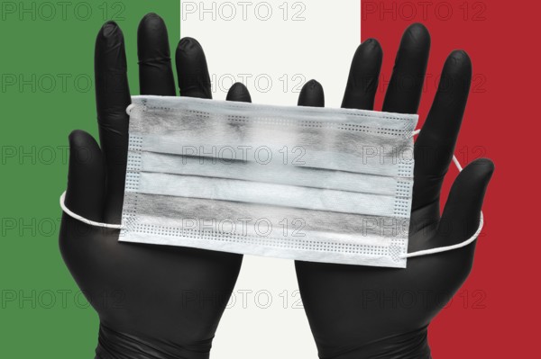 Doctor holds face mask in hands in black medical gloves on background colors flag of Italy or
