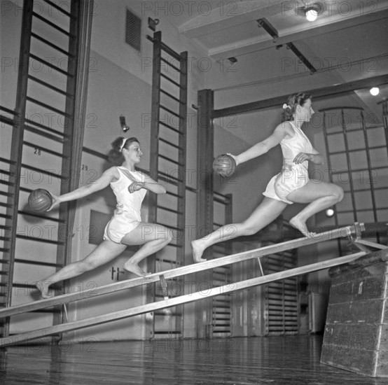 Gymnastics in the 1940s. Two young women are balancing on gymnasium equipment and at the same time