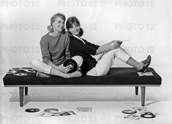1960s lifestyle. Two girls in typical 1960s clothes are sitting together holding music records.