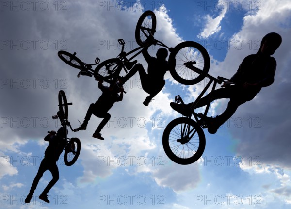 An extreme rider is making a free style jump from a ramp. The young boy with his bicycle is seen as