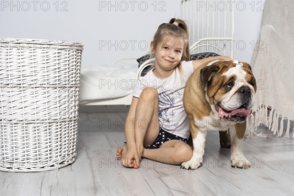 A young girl in a bedroom, sitting on the floor with her dog and stroking him. Child and dog. The