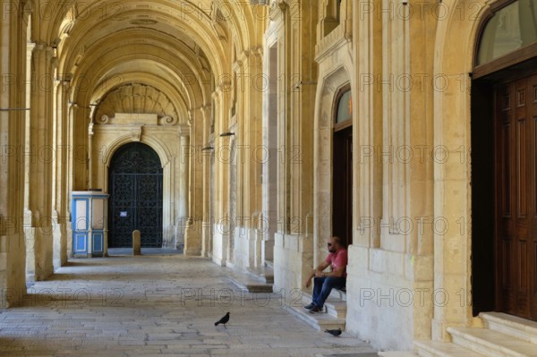 A man with his sandwich and two hungry pigeons in the archway of the National Library, Valletta,
