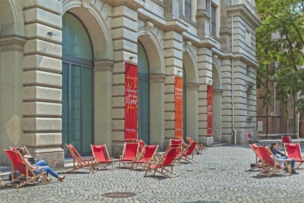 Red deckchairs and advertising banners on cobblestones in front of the Literaturhaus, Munich,