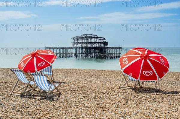Folding chairs with parasols on the beach in front of the ruins of the burnt down West Pier in