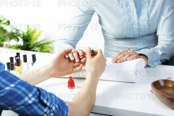 Manicurist working with client's nails at table. Closeup of beautiful female hands applying red