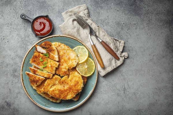 Crispy panko breaded fried chicken fillet with green salad and lemon cut on plate on gray