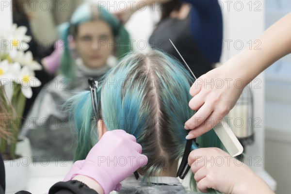 Back view of female head with emerald hair color and regrown hair roots. Woman sits in chair by