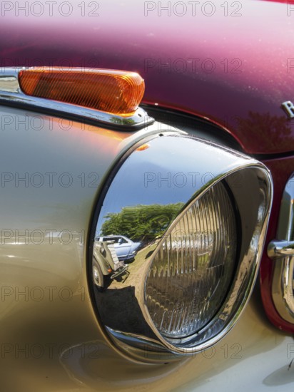 Close-up of a chrome-plated spotlight with reflection of the surroundings on a red background,