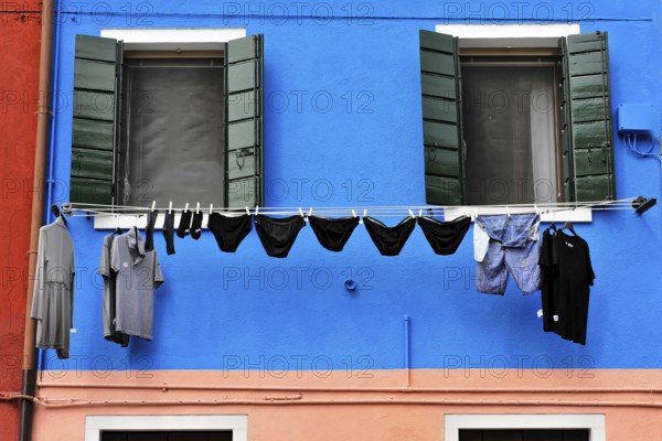Venice, Veneto, Italy, Europe, Vibrant blue façade with green shutters, contrasting clothing on